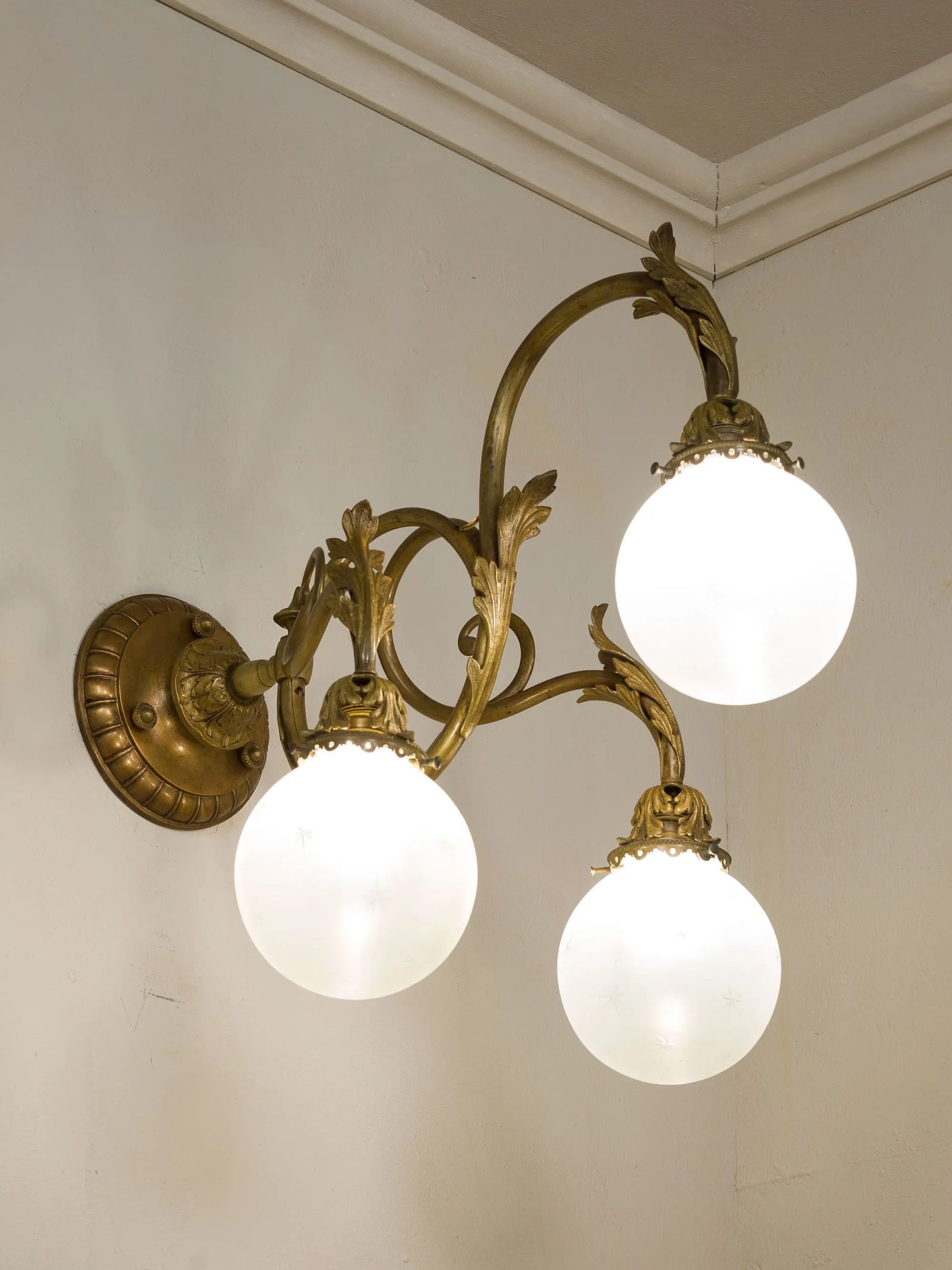 Elegnte lampada a muro Liberty con tre ampi bracci a voluta che sorreggono i globi in vetro satinato | Lo Stile Italiano