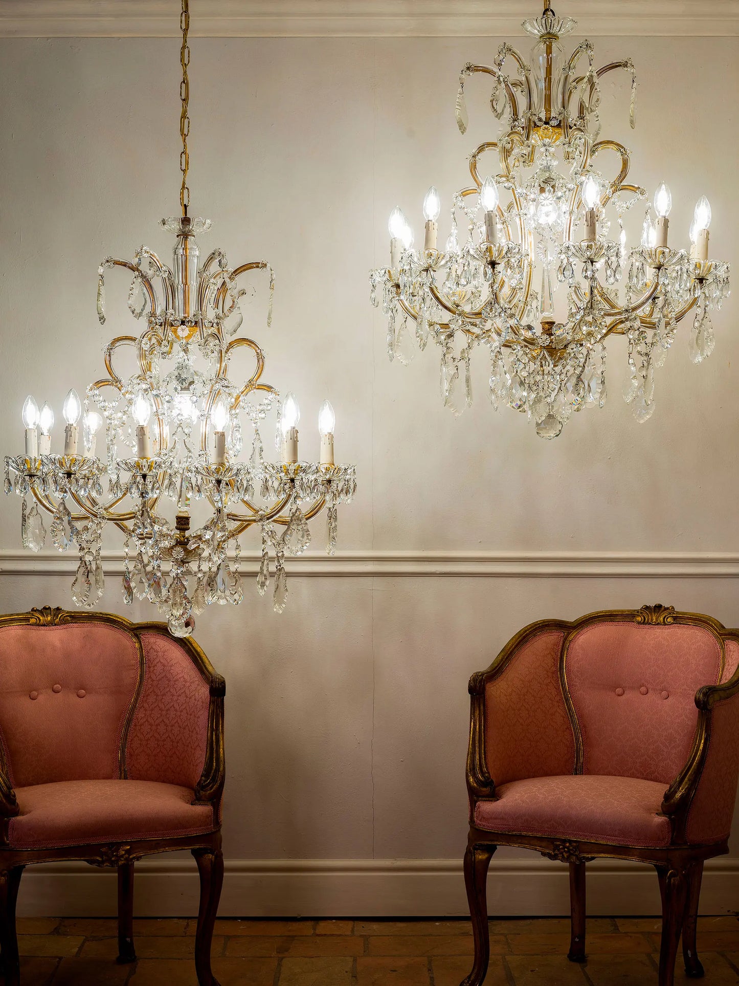 Coppia di lampadari Maria Teresa in cristallo di Boemia, 13 luci, anni ’30-’40, sospesi in una sala elegante con due poltroncine antiche | Lo Stile Italiano