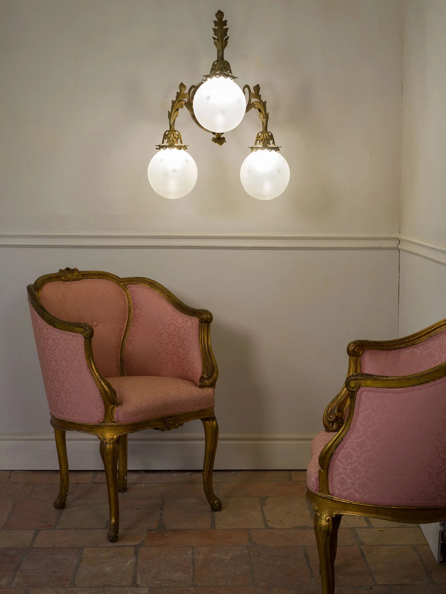 Lampada da parete antica a tre luci in bronzo e globi in vetro, fotografata insieme a una coppia di poltrone Napoleone III. | Lo Stile Italiano