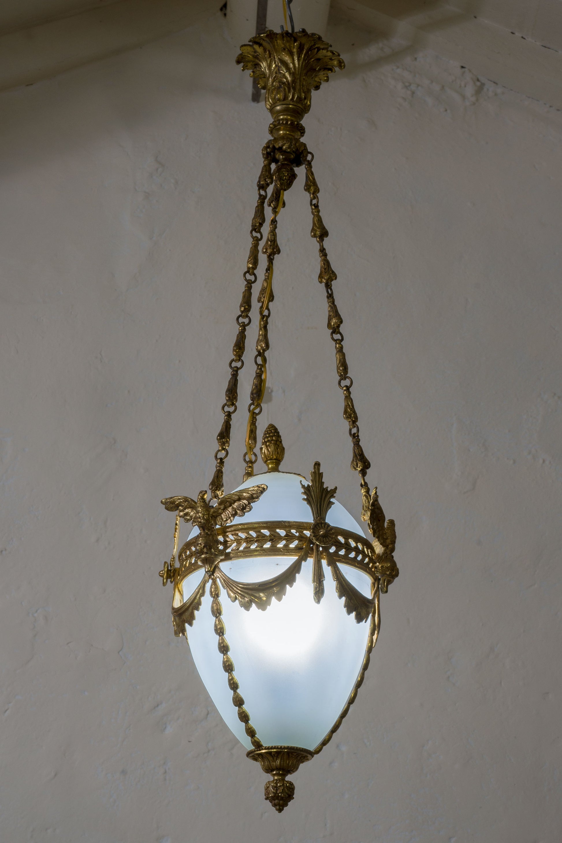 Lampadario in ottone cesellato con al centro un  globo in vetro opalino leggermente azzurrato a forma di uovo. | Lo Stile Italiano