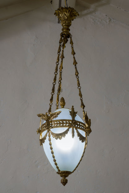 Lampadario in ottone cesellato con al centro un  globo in vetro opalino leggermente azzurrato a forma di uovo. | Lo Stile Italiano