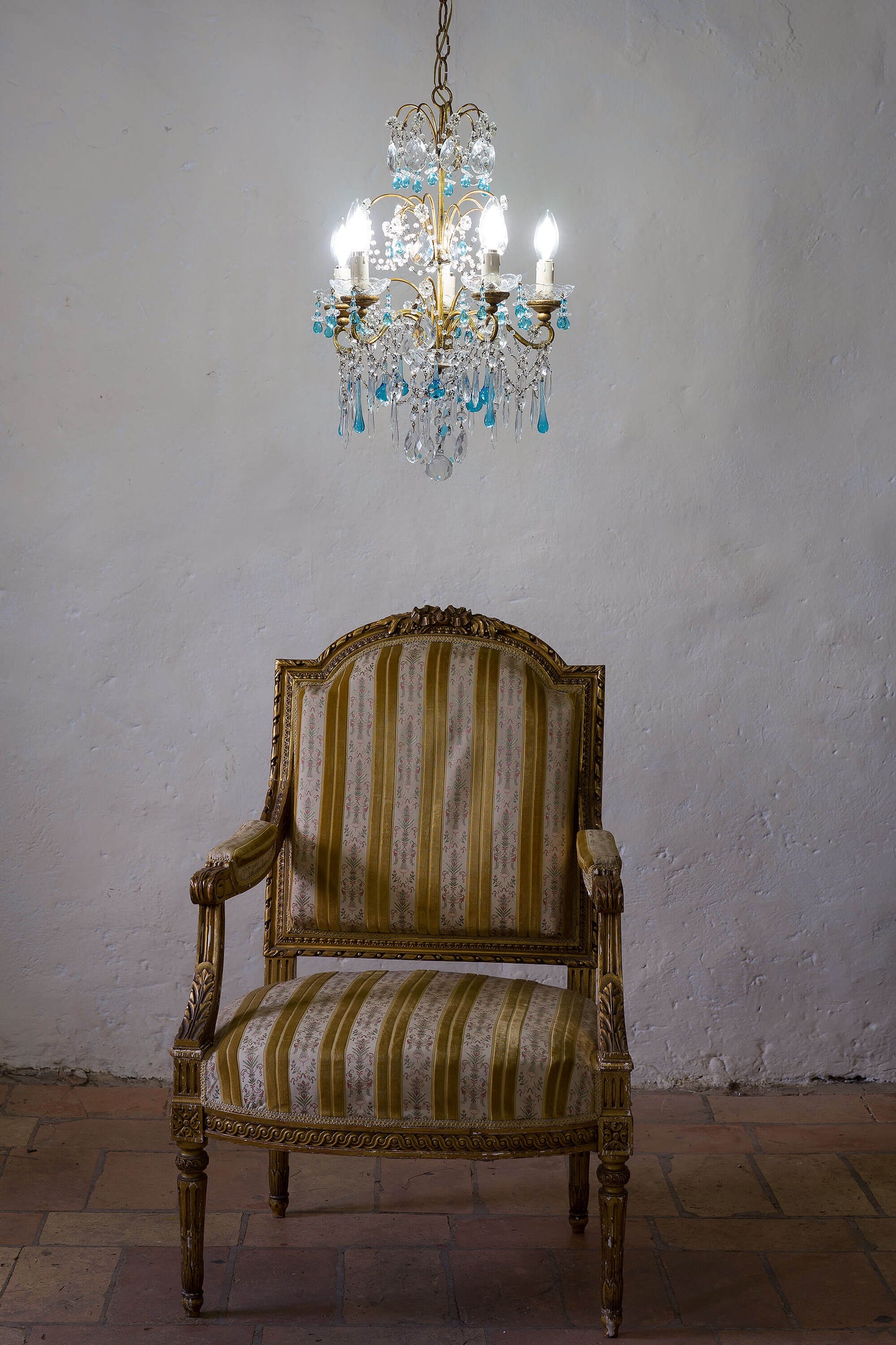 Lampadario Maria Teresa Vintage, con poltrona Luigi XVI in legno dorato e tappezzeria a righe avorio e giallo. | Lo Stile Italiano