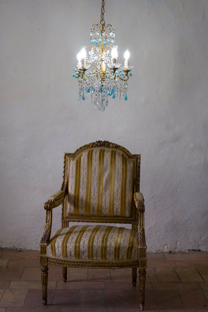 Lampadario Maria Teresa Vintage, con poltrona Luigi XVI in legno dorato e tappezzeria a righe avorio e giallo. | Lo Stile Italiano