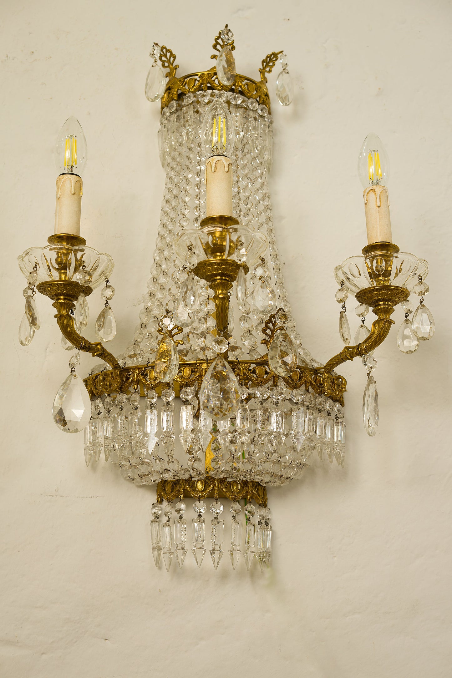 Applique in ottone cesellato e dorato vista frontale, 3 bracci con candela in plastica, gocce di cristallo pendenti-Lo Stile Italiano